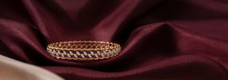 A Réia gold bracelet with a braided design and a line of lab-grown diamonds, draped over a cylindrical white surface.