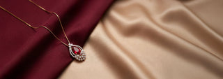 A Réia gold and pearl statement necklace featuring a large ornamental pendant with a dark red stone, white lab-grown diamonds, and a hanging tassel of gold beads, worn on a model's neck.
