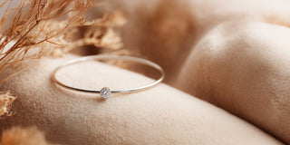A thin gold bangle bracelet with a single line of pavé set lab-grown diamonds is worn on an arm against blue fabric.