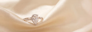 A Réia white gold solitaire ring with a Emerald-cut lab-grown diamond, resting on beige fabric.