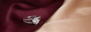 A Reia white gold solitaire engagement ring features a six-prong setting holding a round brilliant lab-grown diamond, resting on textured beige fabric.