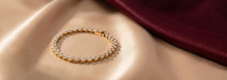 A thin gold chain bracelet with small lab-grown diamonds rests on a block, against a beige background.
