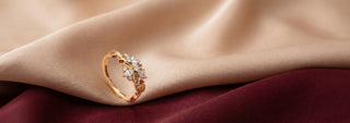 A Réia yellow gold engagement ring with an oval lab-grown diamond in a six-prong setting and diamond accents on the band, resting on beige fabric.