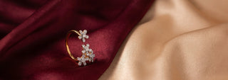 A Réia yellow gold ring with an oval lab-grown diamond center stone and marquise lab-grown diamond side accents, resting on beige fabric with dried flowers.