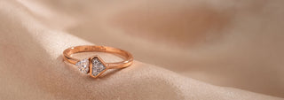 A Reia rose gold wide band ring with a pavé lab-grown diamond braided design, displayed on a pink surface with corner shadows.