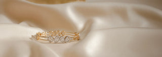 A Réia gold bracelet with a braided design and a line of lab-grown diamonds, draped over a cylindrical white surface.