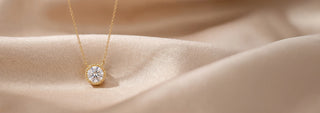 A Réia yellow gold pendant with a lab-grown diamond center stone surrounded by a small diamond halo, worn close to the neck.