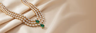 A gold tiered necklace features many small lab-grown diamonds and two large green lab-grown diamonds, on a white surface.