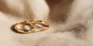 Réia pair of yellow gold wedding bands, one plain and one set with lab-grown diamonds, on beige fabric.