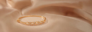 A thin gold chain necklace with five bezel-set lab-grown diamonds rests on a stone slab next to dry grass.