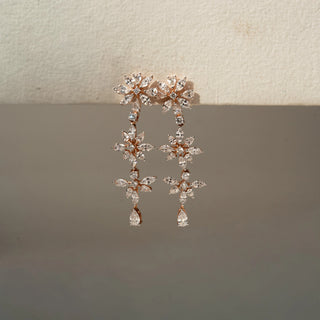 Front view of floral drop earrings in rose gold, featuring marquise-cut lab-grown diamonds arranged in blooming flower motifs with pear-shaped diamond drops. Captured against a neutral beige backdrop.