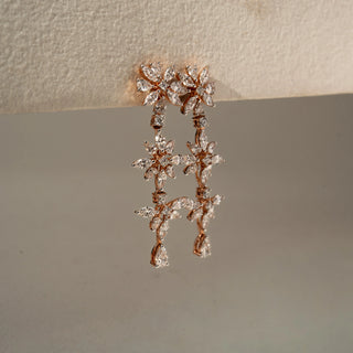 Side view of floral drop earrings in rose gold, featuring marquise-cut lab-grown diamonds arranged in cascading flower motifs with pear-shaped diamond drops. Set against a beige backdrop.