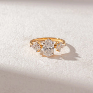 Top view of a yellow gold trilogy ring featuring an oval-cut lab-grown diamond centre stone, flanked by Oval-cut side diamonds. Captured against a beige backdrop, the elegant three-stone design highlights brilliance and balance.