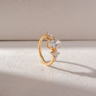 Angled side view of a yellow gold trilogy ring featuring an oval-cut lab-grown diamond centre stone, flanked by trillion-cut side diamonds. Captured against a beige backdrop, the elevated setting highlights brilliance and dimension.