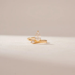 Front view of a 14KT Yellow Gold ring featuring a pear-cut centre diamond and a curved band with a pear-shaped diamond accent.