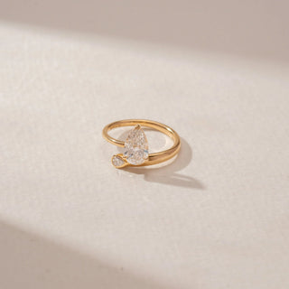 Close-up view of a 14KT Yellow Gold ring featuring a pear-cut centre diamond and a curved band with a pear-shaped diamond accent.