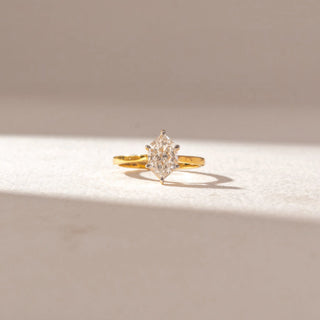 Front view of marquise diamond solitaire ring in yellow gold with a slim band, set on a soft neutral surface, highlighting elongated shape and crisp, radiant brilliance.
