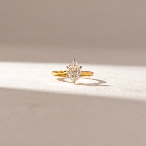 Front view of marquise diamond solitaire ring in yellow gold with a slim band, set on a soft neutral surface, highlighting elongated shape and crisp, radiant brilliance.

