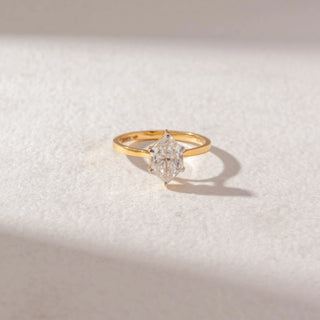 Top view of marquise diamond solitaire ring in yellow gold with a slim band, set on a soft neutral surface, highlighting elongated symmetry and bright, refined sparkle.
