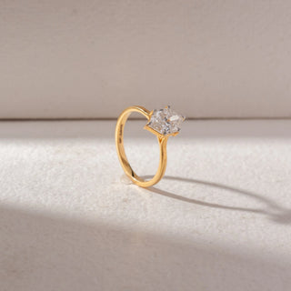 Angled view of marquise diamond solitaire ring in yellow gold with a slim band, set on a soft neutral background, highlighting elevated setting and clean, radiant brilliance.
