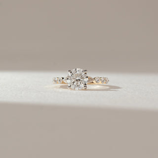 Front view of solitaire diamond ring in yellow gold, featuring a round lab-grown diamond at the centre with marquise and round diamond accents on the band. Set on a soft neutral backdrop, it reflects classic elegance.