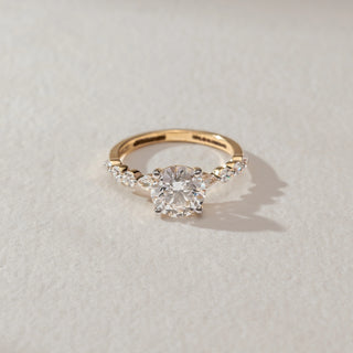 Top view of solitaire diamond ring in yellow gold, featuring a round lab-grown diamond at the centre with marquise and round diamond accents on the band. Set on a soft neutral surface, it reflects classic brilliance.