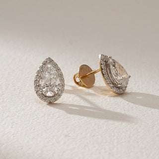 Oval-cut lab-grown diamond halo stud earrings in 18KT Yellow Gold, featuring EF-VVS diamonds with a radiant halo design, displayed on a soft neutral surface with Bombay screw backs.