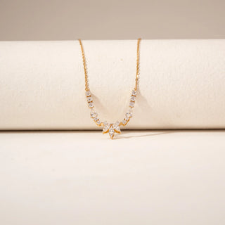 Close-up view of a diamond necklace in 14KT Yellow Gold, featuring a marquise floral pendant and diamond accents against a beige backdrop.