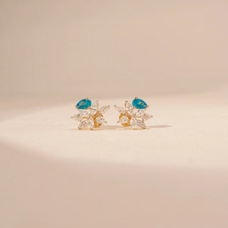 Close-up view of floral diamond earrings in 14KT yellow gold, featuring pear-shaped blue gemstones and marquise-cut lab-grown diamonds.