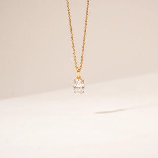 Front view of a diamond pendant in 14KT Yellow Gold, featuring a oval-cut centre stone in a four-prong setting against a beige backdrop.