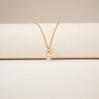 Close-up view of a diamond pendant in 14KT Yellow Gold, featuring a oval-cut centre stone in a four-prong setting against a beige backdrop.