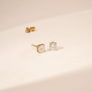 Angled view of square-cut diamond stud earrings in 14KT Yellow Gold, featuring four-prong settings.