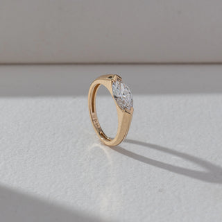 Side view of Marquise Solitaire Diamond Ring in 14KT Yellow Gold, featuring a centred marquise-cut lab grown diamond in prong setting. Set on a beige backdrop, the design highlights structure and sleek elegance.
