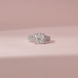Front view of a cushion diamond ring in 14KT White Gold, featuring a pavé-set split band against a soft pink backdrop.