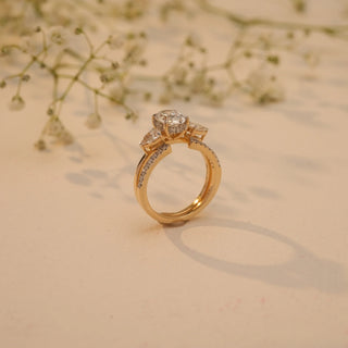 Side view of Reia's Golden Harmony Diamond Bridal Set in 14KT yellow gold, featuring an oval-cut centre diamond with pear accents, captured on a beige floral background.