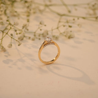 Side view of Reia's Golden Vow Solitaire Diamond Ring in 14KT yellow gold with a round-cut EF-VVS lab-grown diamond, captured on a soft beige floral background.