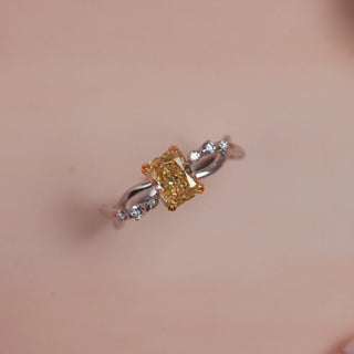 Top view of Reia Sunlit Glow Radiant Diamond Ring on a soft blush-peach background, featuring a radiant-cut yellow lab-grown diamond with white accent stones on a twisted 14KT white gold band.