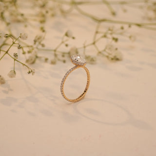 Side view of Reia's Eternal Teardrop Solitaire Diamond Ring in 14KT yellow gold, featuring a pear-cut EF-VVS lab-grown diamond, set against a soft beige floral background.