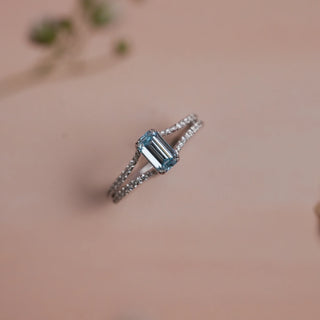 Top view of Reia Azure Emerald-Cut Diamond Ring on a soft blush-peach background, featuring a blue emerald-cut lab-grown diamond set on a split pave band of EF VVS white diamonds in 14KT white gold.