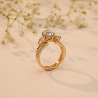 Side view of Reia's Golden Harmony Diamond Bridal Set in 14KT yellow gold, featuring an oval-cut centre diamond with pear accents, captured on a beige floral background.