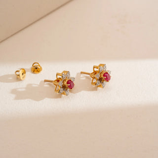 Top-down view of Reia’s 14 KT Yellow Gold Ruby Floral Cluster Diamond Studs with backings. The layout highlights the architectural gold setting and vibrant crimson rubies on a cream backdrop.