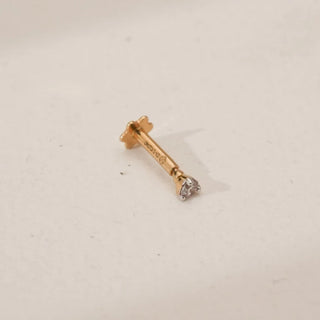 Side view of round solitaire lab-grown diamond nosepin in yellow gold, showing prong-set diamond and straight stem with floral back support on a neutral studio surface.