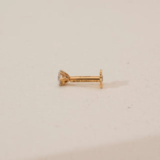 Side profile of yellow gold solitaire diamond nosepin featuring a round lab-grown diamond in a prong setting with straight stem and flat backing, displayed on a neutral studio background.