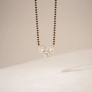 Front view of a diamond mangalsutra in 14KT Yellow Gold, featuring a floral pendant and black bead chain against a beige backdrop.