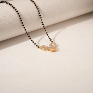 Angled view of a diamond mangalsutra in 14KT Yellow Gold, featuring a floral pendant and black bead chain against a beige backdrop.
