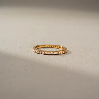 Front view of a diamond eternity band in 14 KT Yellow Gold, featuring a continuous row of round lab-grown diamonds in a classic shared-prong setting, displayed against a beige backdrop.