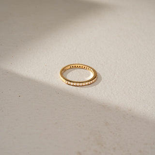 Top view of a diamond eternity band in 14 KT Yellow Gold, featuring a continuous row of round lab-grown diamonds in a classic shared-prong setting, displayed against a beige backdrop.