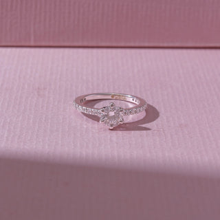 Top view of a white gold diamond ring, featuring a round solitaire center stone with pavé-set band detailing. Captured against a soft pink backdrop, the design reflects timeless sparkle and elegance.