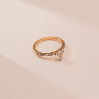 
Top view of Reia’s 18 KT Yellow Gold Forever Heart Diamond Solitaire Ring. A heart-shaped diamond sits on a pavé-set gold band against a soft pink surface, showing its romantic design.