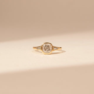 Front view of a 14KT Yellow Gold ring with a bezel-set cushion centre diamond and baguette side diamonds.